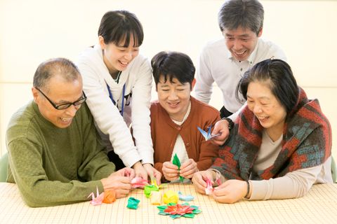 折り紙を折る三人の高齢者と支援する二人のスタッフ
