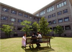 油山病院の中庭の写真でくつろぐ患者二人と話しかけるスタッフ