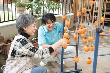 生活リハビリテーションとして干し柿をみる女性とスタッフ